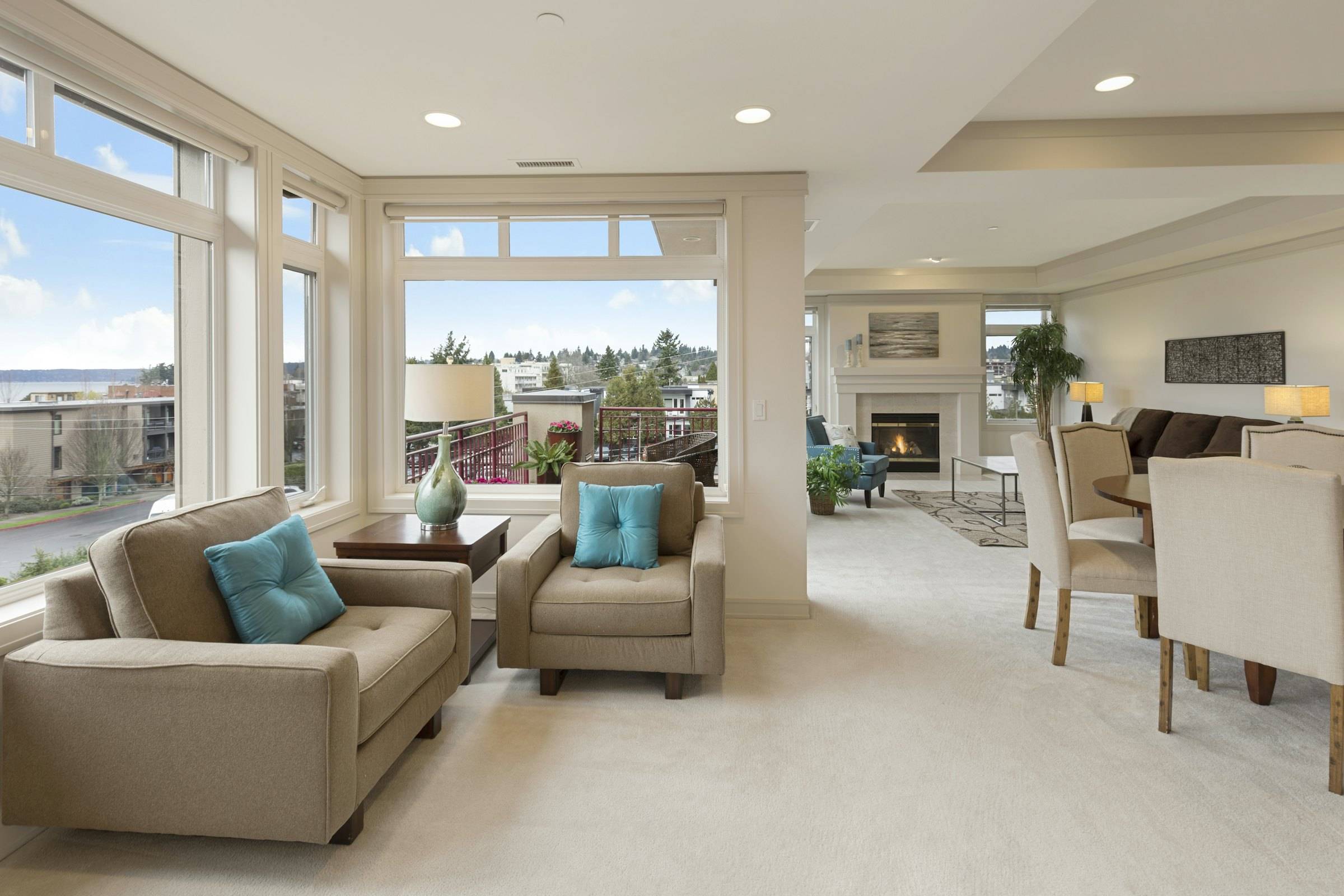 Living room with two beige armchairs, large corner windows and a dining table