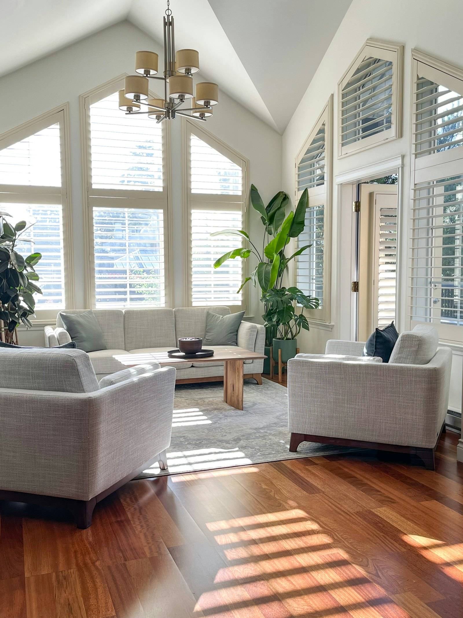 Bright living room with cream sofas under tall windows, sun across the wood floor